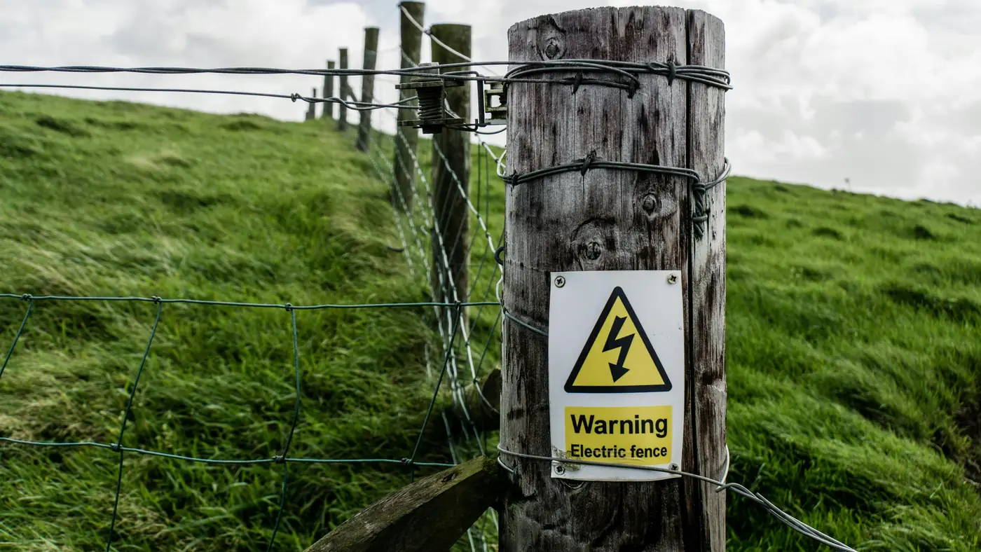 Wooden fence post with an electric fence warning sign on a grassy hillside