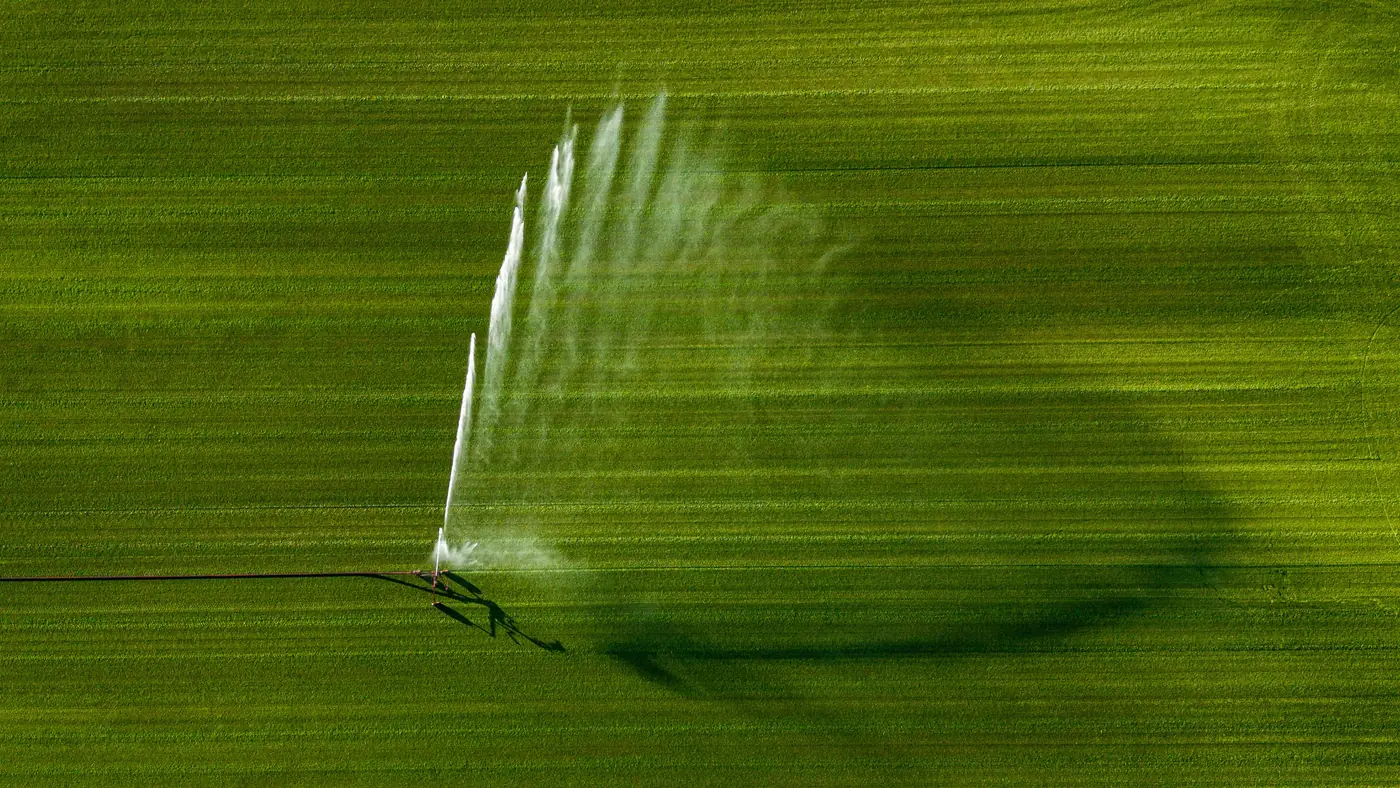 Aerial view of a sprinkler irrigating a green field