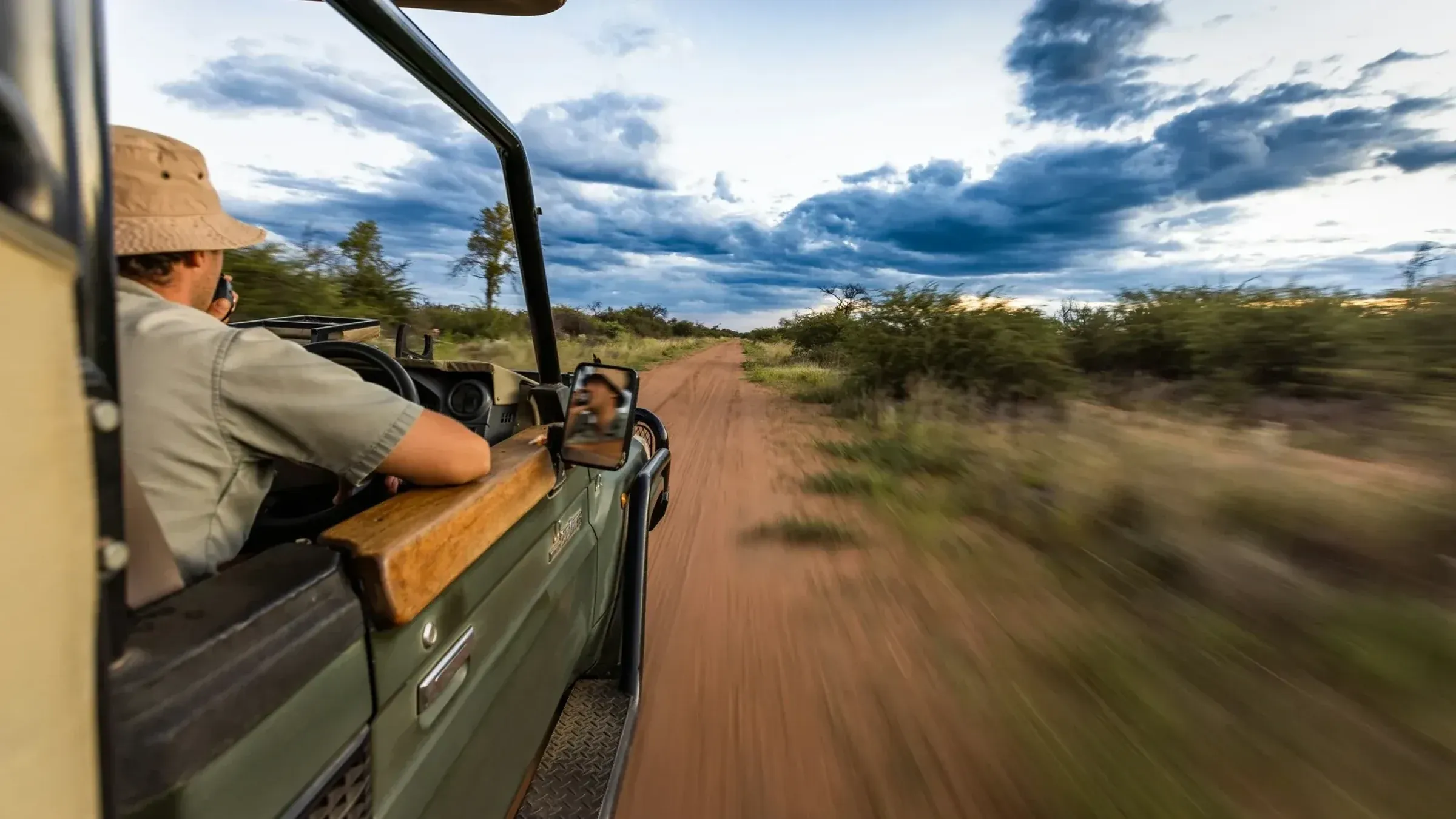 Ranger on radio while driving an open vehicle along a dirt road at dusk